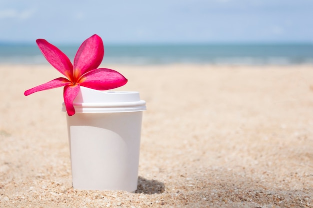 Una tazza di caffè con fiore sulla sabbia contro il paesaggio del mare. Foto di alta qualità