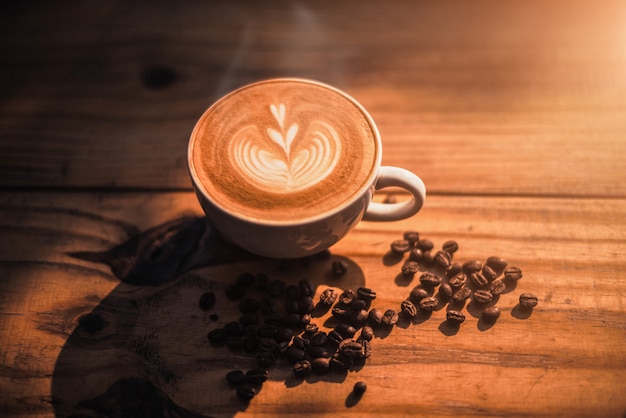 Una tazza di caffè con il modello del cuore in una tazza bianca sul fondo di legno della tavola