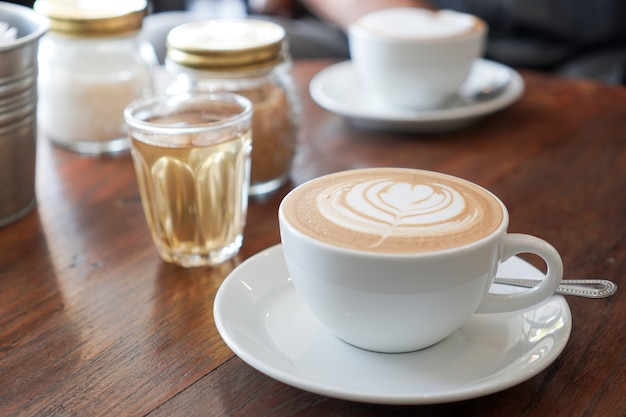 Una tazza di caffè con il modello della foglia in una tazza bianca su fondo di legno.