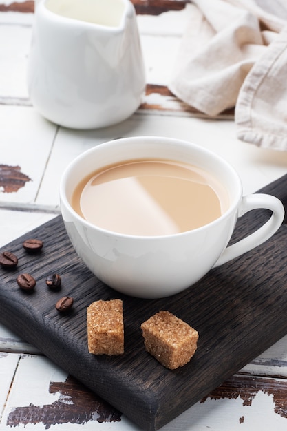 Una tazza di caffè con latte e cubetti di zucchero di canna su un tavolo di legno