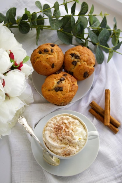 Una tazza di caffè con panna montata accanto a un piatto su cui ci sono dei muffin con la parte superiore del cioccolato vie