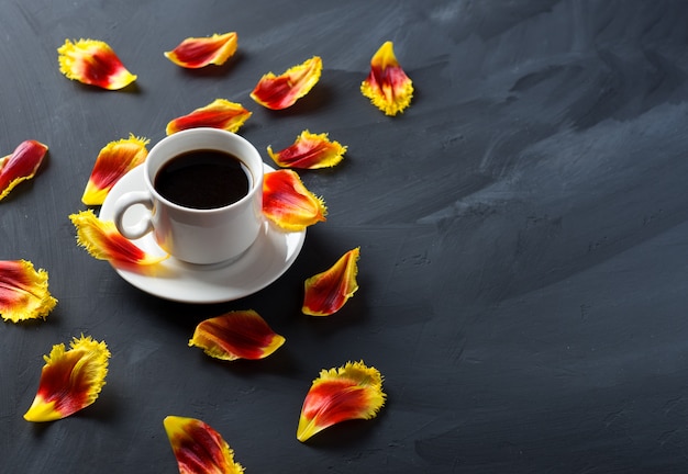 Una tazza di caffè e petali di tulipano sparsi sul tavolo di pietra