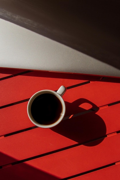 Una tazza di caffè e un laptop su un tavolo rosso Tipo di luce Vista dall'alto con ombre di luce dura
