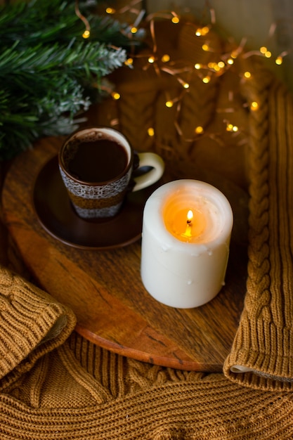 una tazza di caffè e una candela su una lavagna su un maglione caldo accogliente e un rametto di un albero di Natale