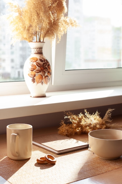 Una tazza di caffè, fiori secchi, barankis, blocco note sulla tavola di legno. Marrone e bianco.