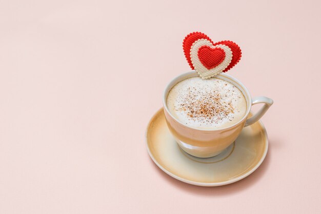 Una tazza di caffè fresco con cannella e panna su una superficie rosa