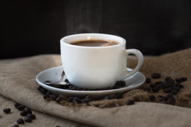 Una tazza di caffè fumante con chicchi di caffè sul tavolo di legno d'epoca.