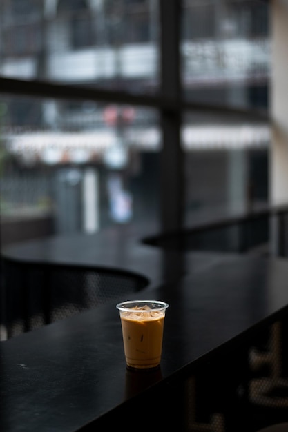 Una tazza di caffè ghiacciato si trova su un bancone nero davanti a una finestra.