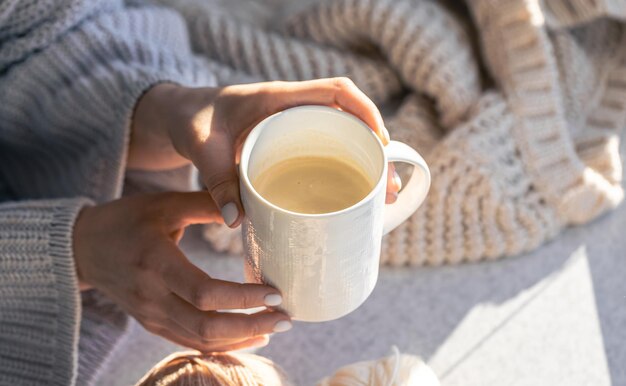 Una tazza di caffè in mano femminile su uno sfondo sfocato con un elemento a maglia