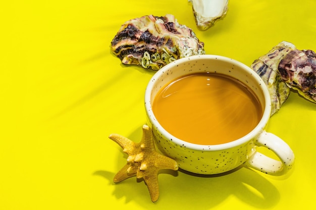 Una tazza di caffè in stile marino Ostriche stelle marine foglie di palma Luce dura ombra scura sfondo giallo brillante spazio piatto per la copia