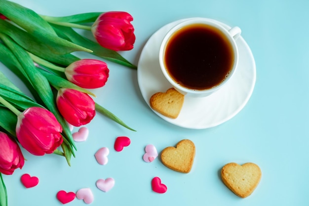 Una tazza di caffè in una tazza bianca con cuori sparsi e tulipani rossi su sfondo blu