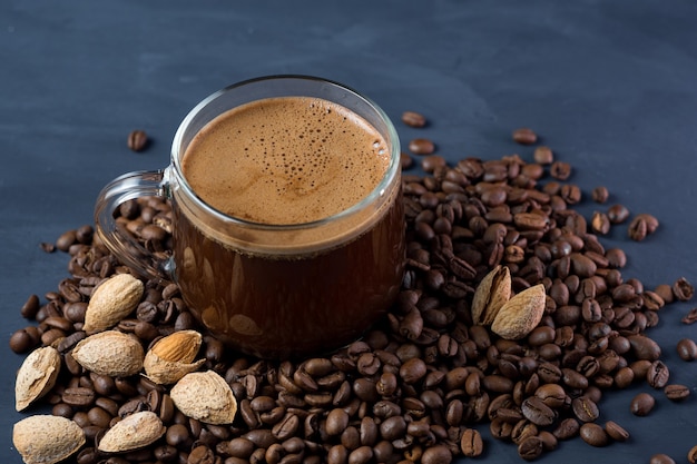 Una tazza di caffè in vetro con mandorle tostate grattugiate su un tavolo di cemento e chicchi tostati sparsi