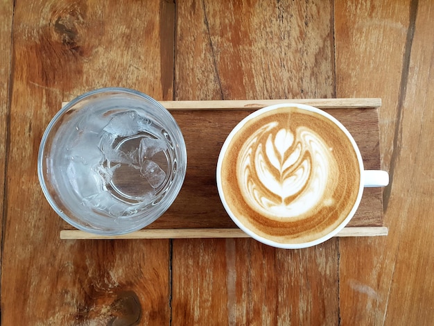 Una tazza di caffè latte art con acqua potabile su fondo di legno.