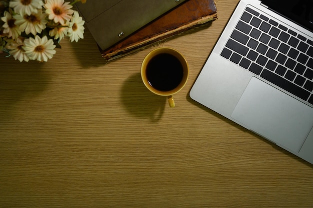 Una tazza di caffè libri vaso di fiori e computer portatile su tavola di legno Semplice spazio di copia sul posto di lavoro per il testo