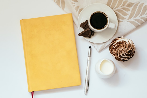 Una tazza di caffè nero con cioccolato e cupcakes e un blocco note