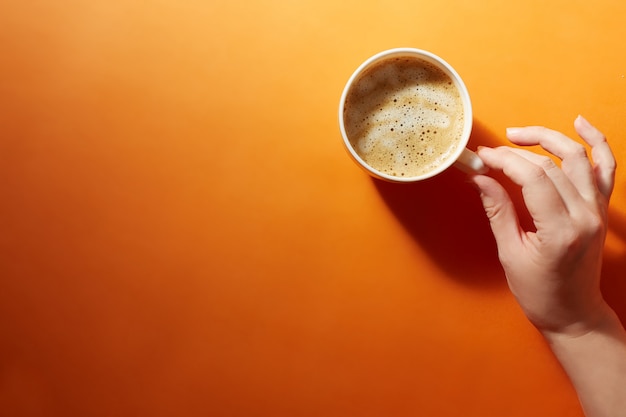 Una tazza di caffè nero con una mano femmina su uno sfondo arancione brillante. Minimalismo, vista dall'alto. copyspace