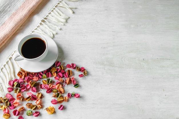 Una tazza di caffè nero e fiori secchi sono posti su un tavolo bianco.