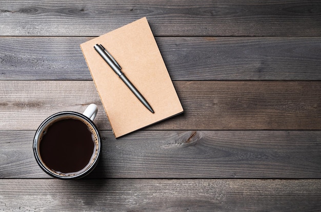 Una tazza di caffè nero e un blocco note artigianale su un vecchio sfondo di legno Concetto di materiali naturali pianificazione del viaggio casa e ufficio posto di lavoro Vista dall'alto e spazio di copia