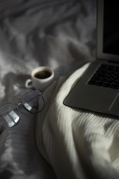 Una tazza di caffè occhiali da laptop sullo sfondo di un letto bianco e un plaid leggero relax e c