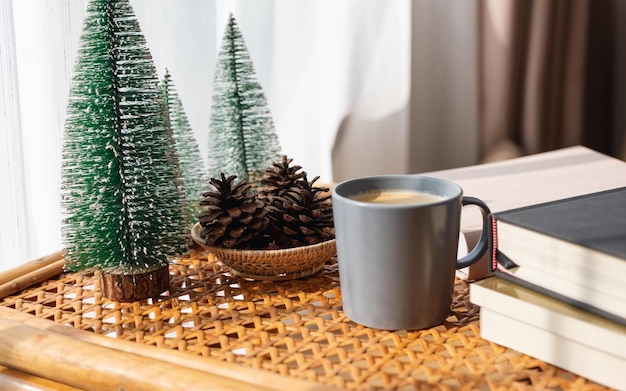 Una tazza di caffè prenota piccoli pini e pigne sul tavolo di legno a casa