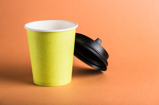 Una tazza di caffè riutilizzabile di carta verde con un coperchio nero aperto.