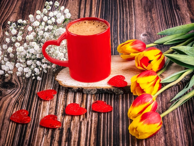 Una tazza di caffè rosso con un cuore un bouquet di tulipani e gypsophila Buon Valentino