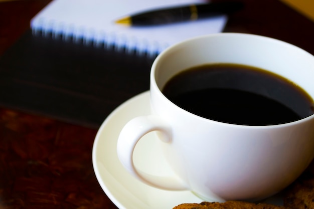 Una tazza di caffè rotondi biscotti su un piattino accanto a un blocco note con una penna il lavoro inizia con la colazione