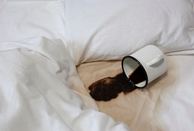 Una tazza di caffè rovesciata sul letto Una tazza è caduta accidentalmente su un lenzuolo bianco Cattiva colazione cattiva Un punto umido