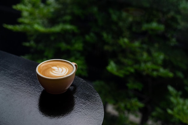 Una tazza di caffè si trova su un tavolo davanti a uno sfondo verde.