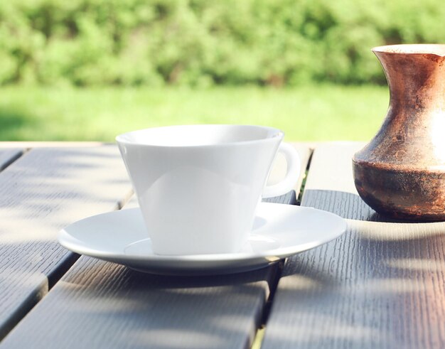 Una tazza di caffè si trova su un tavolo di legno in giardino Dietro c'è un turco con caffè appena fatto