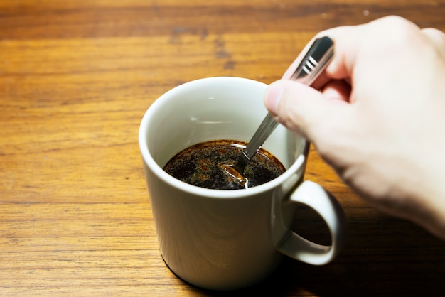 Una tazza di caffè su fondo e sulla mano di legno che tengono un cucchiaio con lo spazio della copia