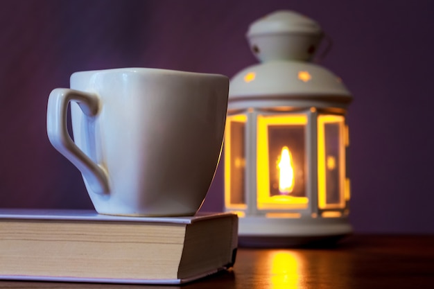 Una tazza di caffè su un libro alla luce di una lanterna con una candela