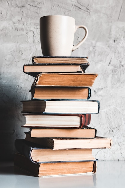Una tazza di caffè su una pila di libri su sfondo grigio. educazione, studio, hobby, lettura