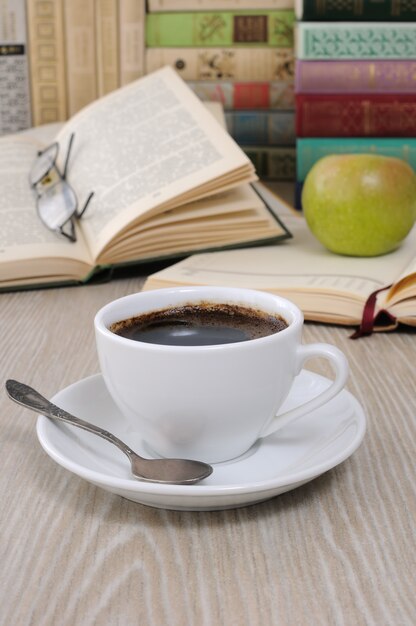 Una tazza di caffè sul tavolo sullo sfondo di un libro aperto con un taccuino