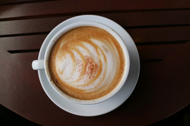 Una tazza di cappuccino caldo con arte del latte sulla tavola di legno. Messa a fuoco selettiva con spazio di copia. Concetto di cibi e bevande.