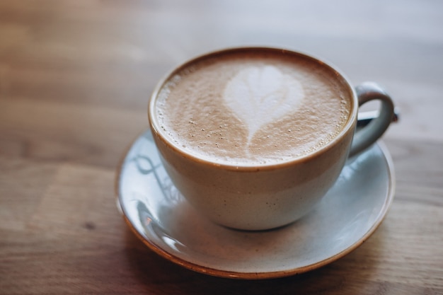 Una tazza di cappuccino con latte art sulla tavola di legno, tazza in ceramica bianca. Cultura del caffè.