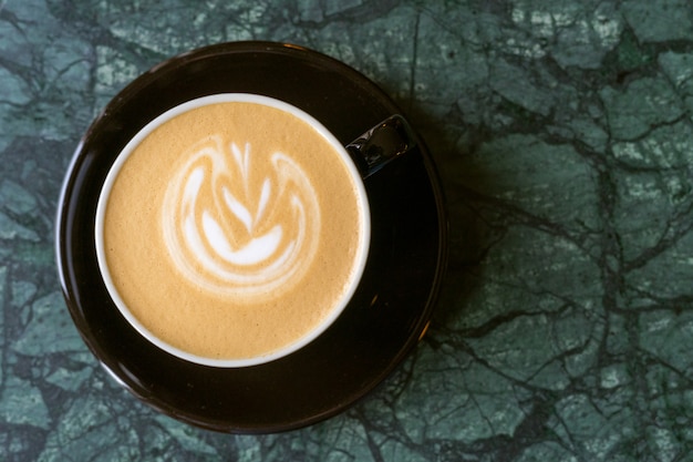 Una tazza di cappuccino con schiuma su un tavolo di marmo in un piccolo caffè accogliente.