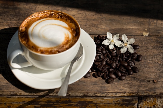 Una tazza di cappuccino e chicchi di caffè su fondo in legno vecchio