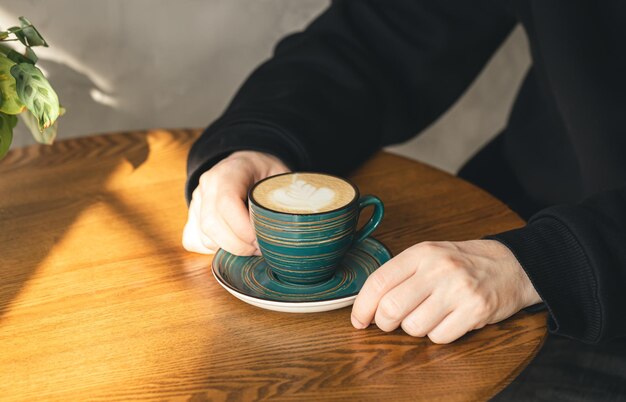 Una tazza di cappuccino in mani maschili in un primo piano del caffè