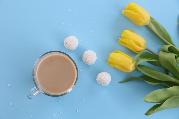 Una tazza di caramelle di caffè e tulipani gialli su sfondo blu