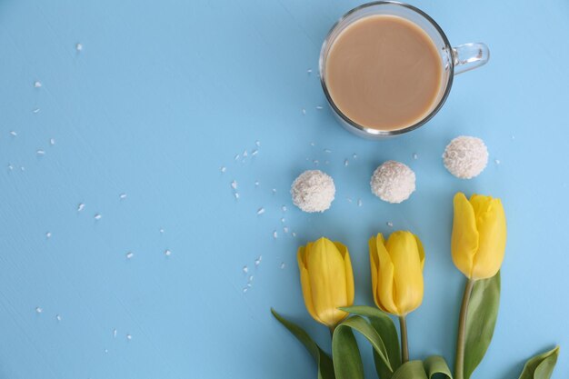 Una tazza di caramelle di caffè e tulipani gialli su sfondo blu