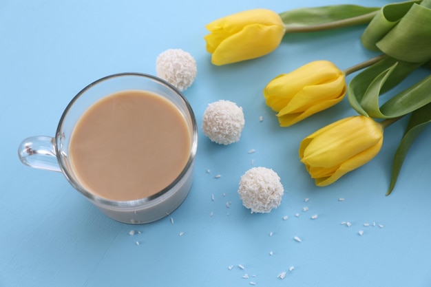 Una tazza di caramelle di caffè e tulipani gialli su sfondo blu