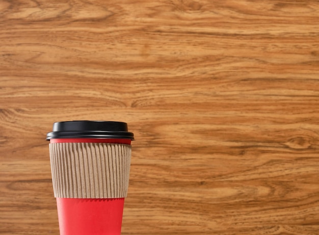 Una tazza di carta da caffè rossa da asporto con un coperchio nero e una copertina di cartone su uno sfondo di legno Copia lo spazio per il testo