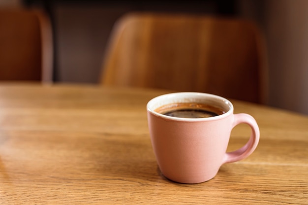 Una tazza di ceramica rosa di caffè nero caldo su una tavola di legno, caffè, spazio della copia