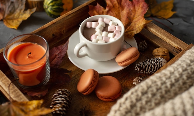 Una tazza di cioccolata calda con marshmallow su un vassoio di legno con pigne di amaretti e foglie cadute