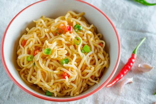 Una tazza di noodles istantanei posizionati su un tavolo di legno con peperoncino come ingredienti, vista dall'alto