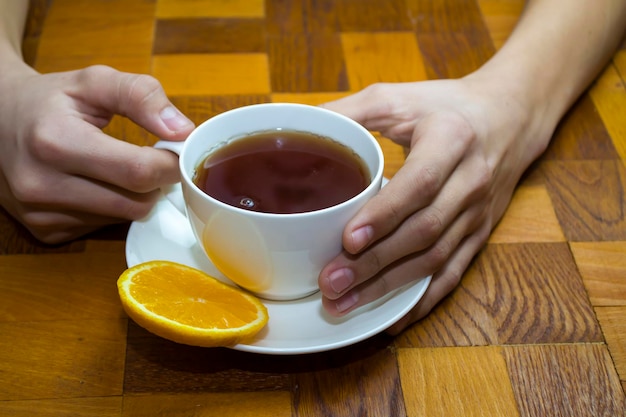 Una tazza di tè bianca nelle sue mani su un tavolo di legno. Foto di alta qualità