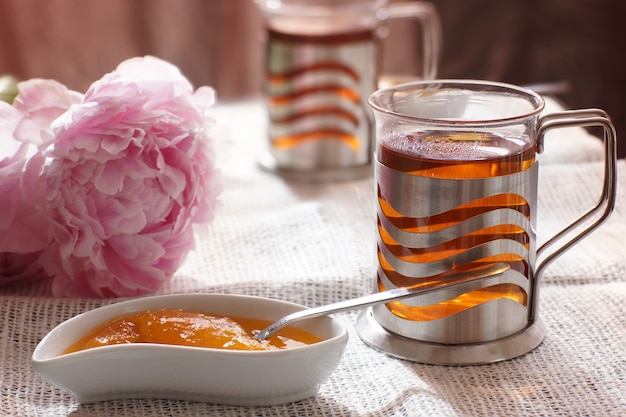 Una tazza di tè caldo accanto a un piattino con dessert e fiori di peonia, colazione per due