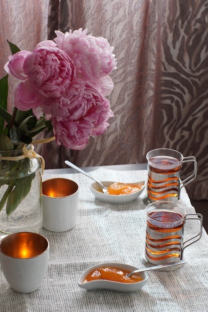 Una tazza di tè caldo accanto a un piattino con dessert e un bouquet di peonie, colazione per due