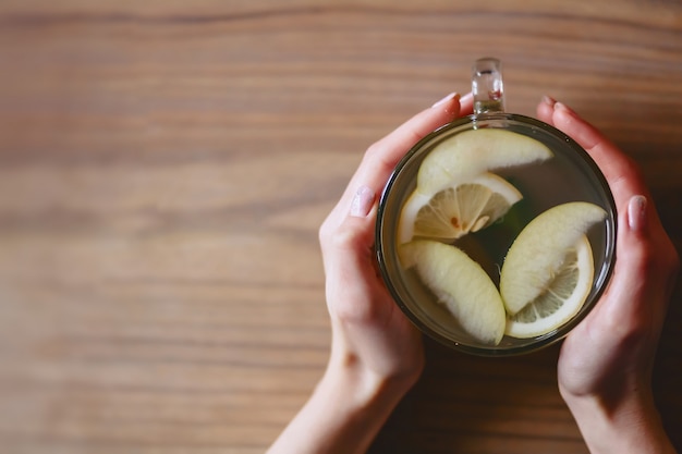 Una tazza di tè caldo con menta e limone nelle mani delle donne